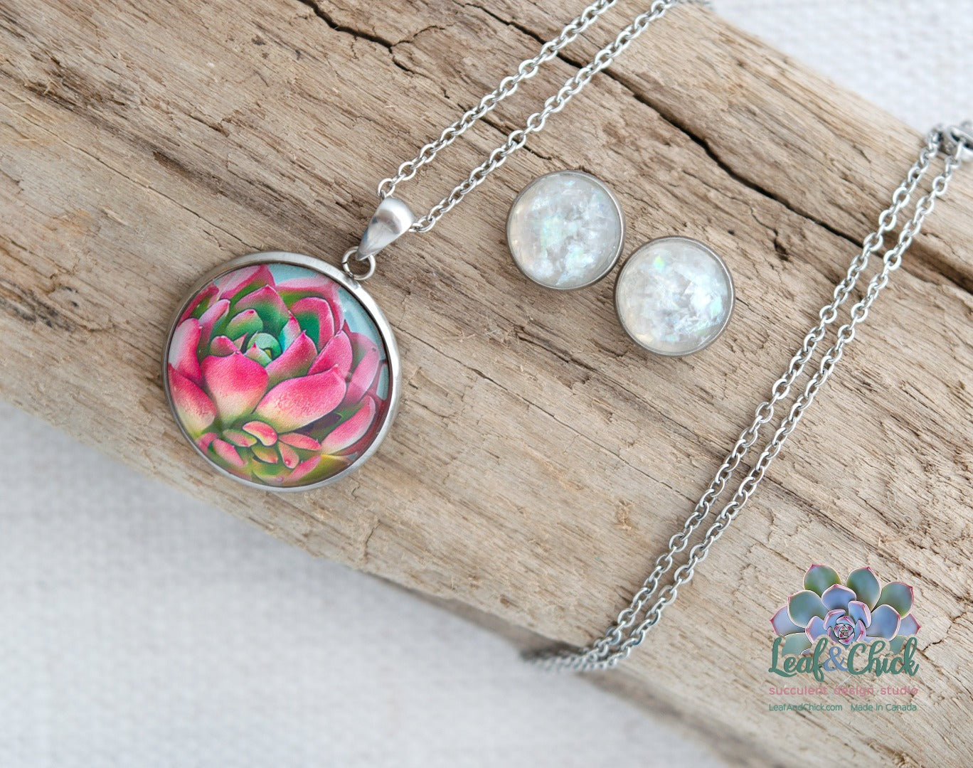 A closeup of a circular bright pink succulent art necklace and small stud earrings